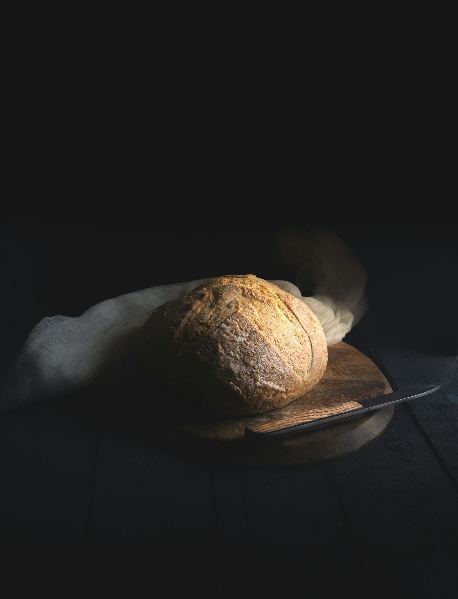 A scored sourdough loaf with deep, blistered crust on a wooden board, lit by warm morning light